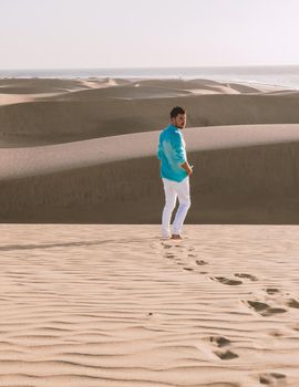 Young men walking at the beach of Maspalomas Gran Canaria Spain, men at the sand dunes desert of Maspalomas Gran Canaria during a vacation in Spain