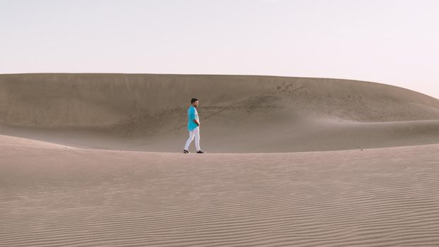 Young men walking at the beach of Maspalomas Gran Canaria Spain, young men walking in de sand during sun rise in the desert of Maspalomas Gran Canaria