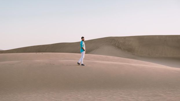 Young men walking at the beach of Maspalomas Gran Canaria Spain, young men walking in de sand during sun rise in the desert of Maspalomas Gran Canaria