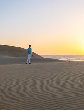 Young men walking at the beach of Maspalomas Gran Canaria Spain, young men walking in de sand during sun rise in the desert of Maspalomas Gran Canaria