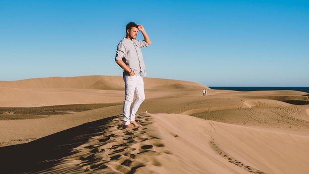 Young men walking at the beach of Maspalomas Gran Canaria Spain, men at the sand dunes desert of Maspalomas Gran Canaria during a vacation in Spain