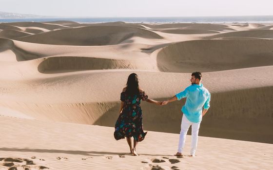 A couple walking at the beach of Maspalomas Gran Canaria Spain, men and woman at the sand dunes desert of Maspalomas Gran Canaria during vacation in Spain