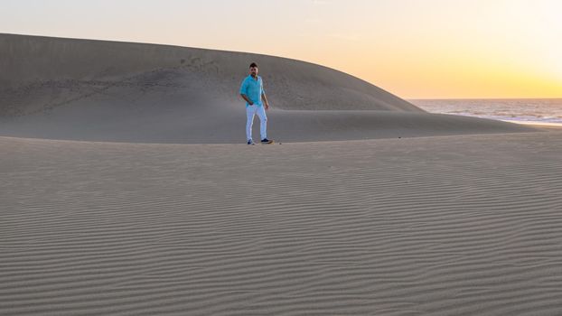 Young men walking at the beach of Maspalomas Gran Canaria Spain, young men walking in de sand during sun rise in the desert of Maspalomas Gran Canaria