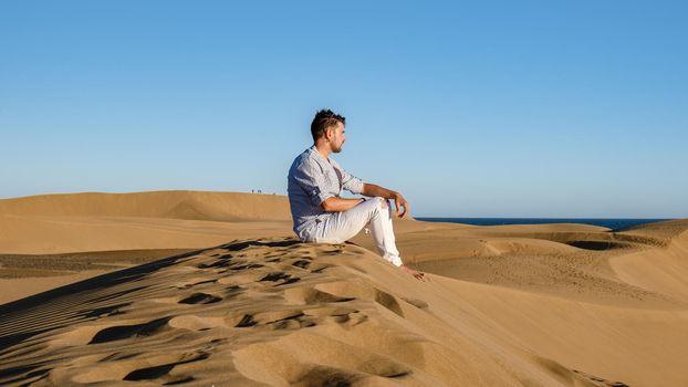 Young men walking at the beach of Maspalomas Gran Canaria Spain, young men walking in de sand during sun rise in the desert of Maspalomas Gran Canaria