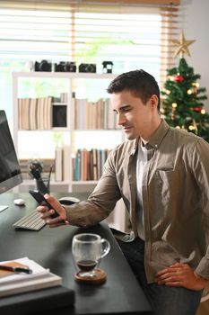 Young man sitting in front of computer and using mobile phone.