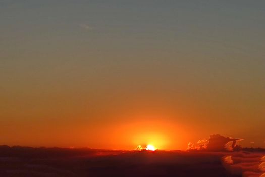 orange sunrise over clouds on dark morning sky.