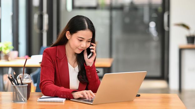 Businesswoman working with computer laptop and talking on mobile phone with with business partner.