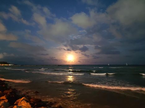 bright full moon in a stormy sky over the sea horizon, lunar path.