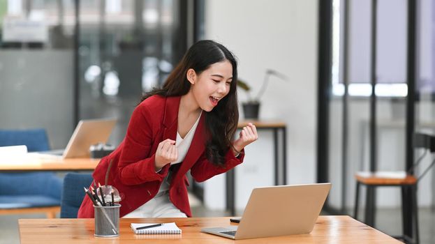 Happy businesswoman standing at her workplace and celebrating successful project.