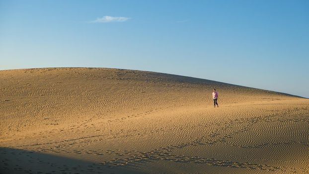 Young men walking at the beach of Maspalomas Gran Canaria Spain, young men walking in de sand during sun rise in the desert of Maspalomas Gran Canaria