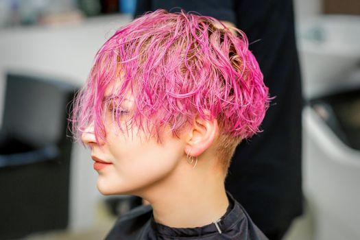 Beautiful young caucasian woman receiving new short pink hairstyle in hairdresser salon