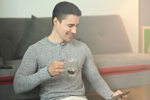 Smiling handsome man drinking coffee and surfing internet in living room.