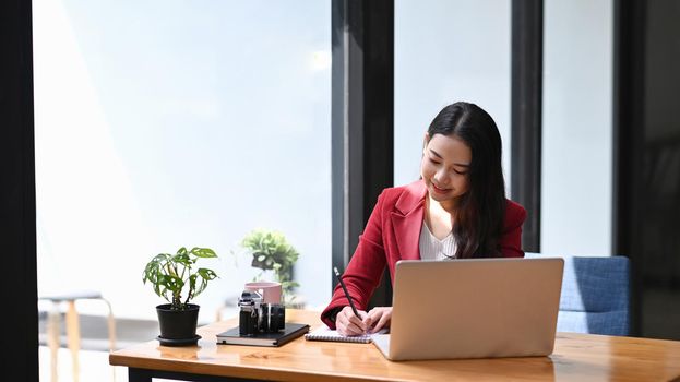 Young female entrepreneur sitting in modern workplace and working with laptop computer.