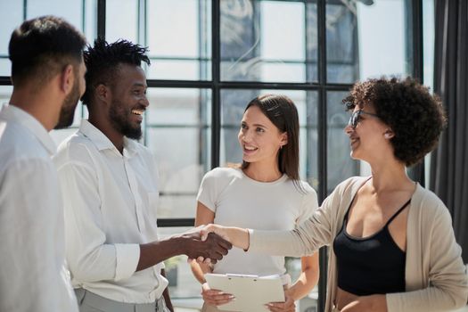 Glad to work with you. Young modern men in smart casual wear shaking hands and smiling while working in the creative office