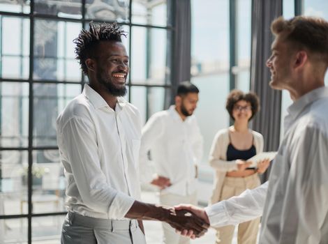 Glad to work with you. Young modern men in smart casual wear shaking hands and smiling while working in the creative office