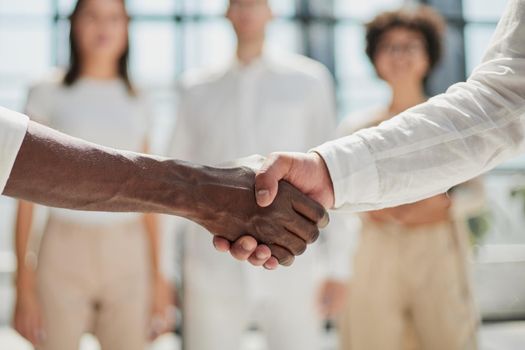 Glad to work with you. Young modern men in smart casual wear shaking hands and smiling while working in the creative office