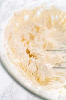 Mixing ingredients in a large glass mixing bowl to prepare cream cheese frosting.