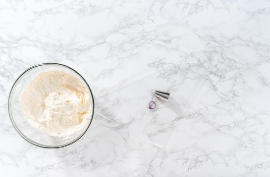 Flat lay. Whisking buttercream frosting in a glass mixing bowl with an electric hand mixer to prepare the peppermint buttercream frosting.