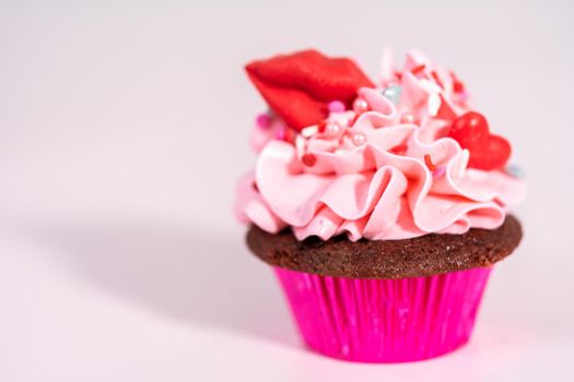 Red velvet cupcakes with pink Italian buttercream frosting and decorates with heart and kiss shaped red chocolates.