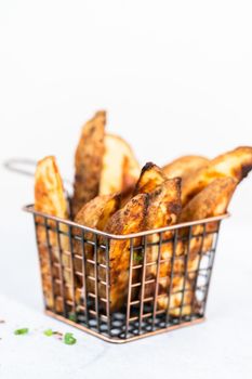 Freshly baked potato wedges with spices in a wire basket.