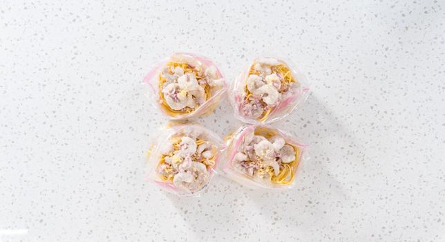 Flat lay. Packaging homemade frozen shrimp scampi meal prep into plastic resealable bags.