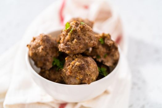 Homemade oven-baked meatballs in a glass serving bowl.
