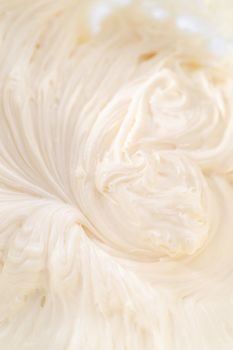 Mixing ingredients in a large glass mixing bowl to prepare cream cheese frosting.