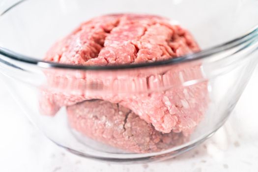 Mixing ingredients with a potatoe masher in a glass mixing bowl to prepare oven-baked meatballs.