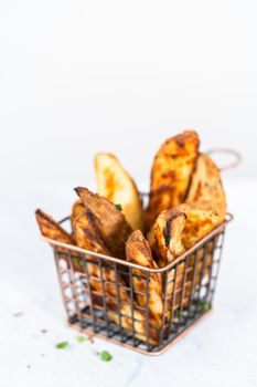 Freshly baked potato wedges with spices in a wire basket.