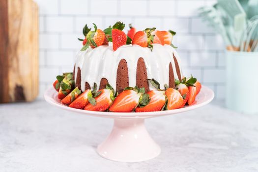 fresh strawberries..Red velvet bundt cake with cream cheese frosting garnished with fresh strawberries on a pink cake stand for Valentines Day.