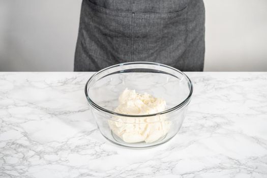 Whisking buttercream frosting in a glass mixing bowl with an electric hand mixer to prepare the peppermint buttercream frosting.