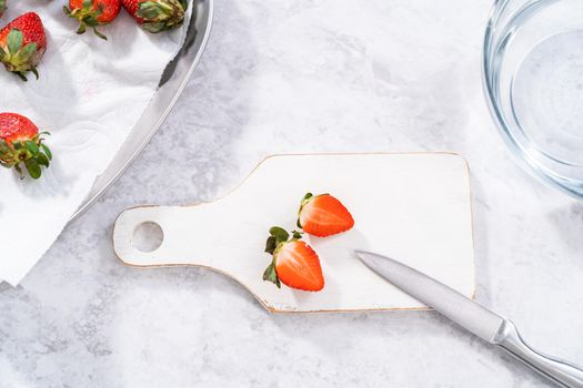 Slicing fresh organic strawberries on a white cutting board.