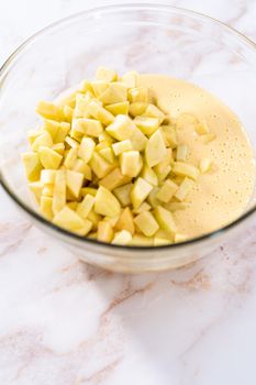 Mixing ingredients in a large glass mixing bowl to bake apple sharlotka muffin.