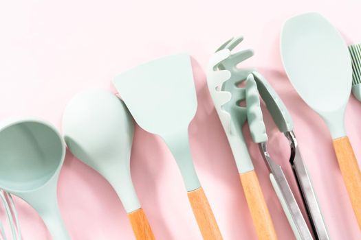 New blue silicone kitchen utensils with wooden handles on a pink background.