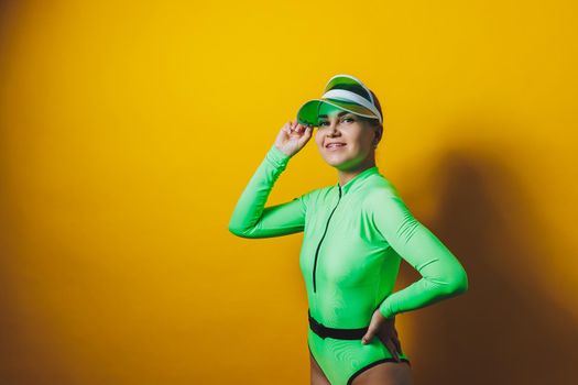 Attractive woman in bright green beach swimsuit, hat, on bright yellow background with perfect body. Isolated. Studio shot.