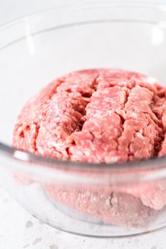 Mixing ingredients with a potatoe masher in a glass mixing bowl to prepare oven-baked meatballs.