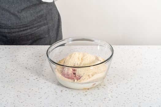 Mixing ingredients with a potatoe masher in a glass mixing bowl to prepare oven-baked meatballs.