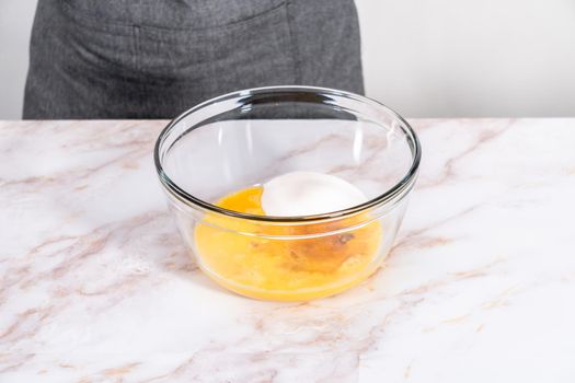 Mixing ingredients in a large glass mixing bowl to bake apple sharlotka muffin.