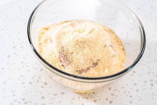 Mixing ingredients with a potatoe masher in a glass mixing bowl to prepare oven-baked meatballs.
