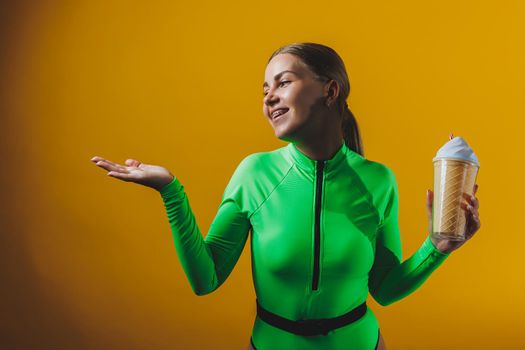 A smiling woman in a green swimsuit with a cocktail in her hands is happy about the upcoming vacation, isolated on a bright yellow background. Summer tropics travel concept.