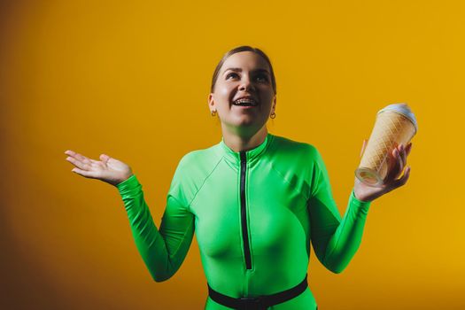 A smiling woman in a green swimsuit with a cocktail in her hands is happy about the upcoming vacation, isolated on a bright yellow background. Summer tropics travel concept.