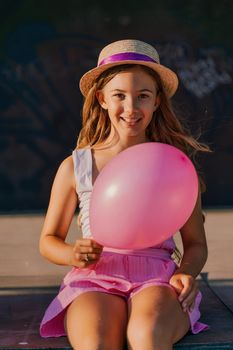 Portrait of a girl in a hat with a pink balloon. She is dressed in pink clothes and her hair is long and loose