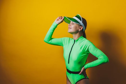 Attractive woman in bright green beach swimsuit, hat, on bright yellow background with perfect body. Isolated. Studio shot.