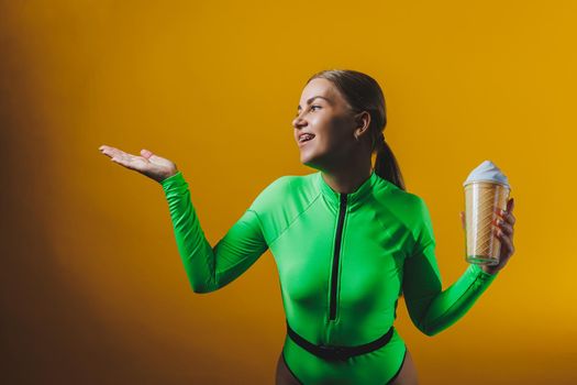 A smiling woman in a green swimsuit with a cocktail in her hands is happy about the upcoming vacation, isolated on a bright yellow background. Summer tropics travel concept.