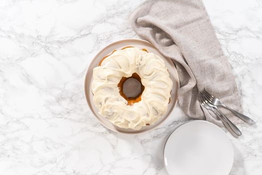 Flat lay. Freshly baked pumpkin bunt cake with cream cheese frosting on the kitchen counter.