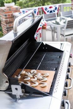 Grilling shrimp on a grill mat over an outdoor gas grill.