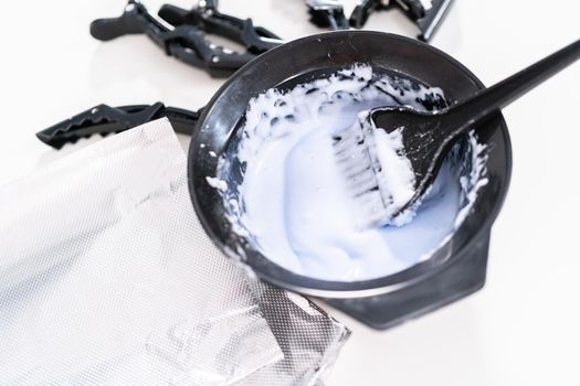 Mixing hair color dye in a black mixing bowl with a brush.