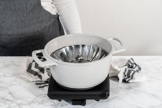 Steaming fresh broccoli in a cooking pot with a steamer basket to prepare steamed broccoli.