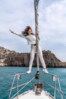 Woman standing on the nose of the yacht at a sunny summer day, breeze developing hair, beautiful sea on background.