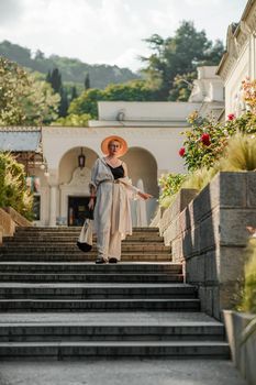 Woman on the stairs in the park. A middle-aged lady in a hat in a white outfit with a bag walks around the Livadia Palace.